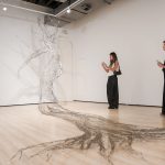 A stainless-steel tree drawn across the gallery floor and wall, with visitors