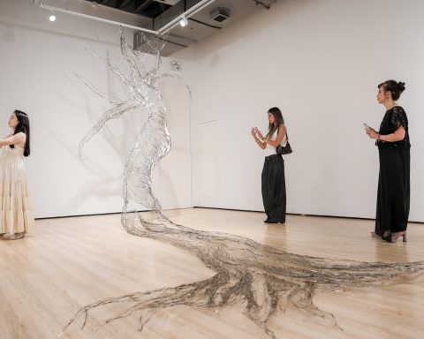 A stainless-steel tree drawn across the gallery floor and wall, with visitors