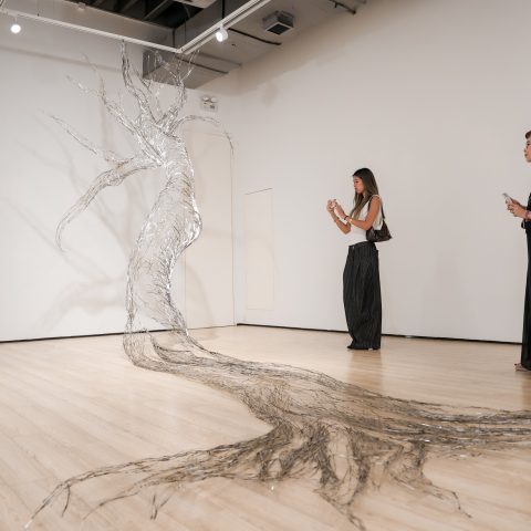 A stainless-steel tree drawn across the gallery floor and wall, with visitors