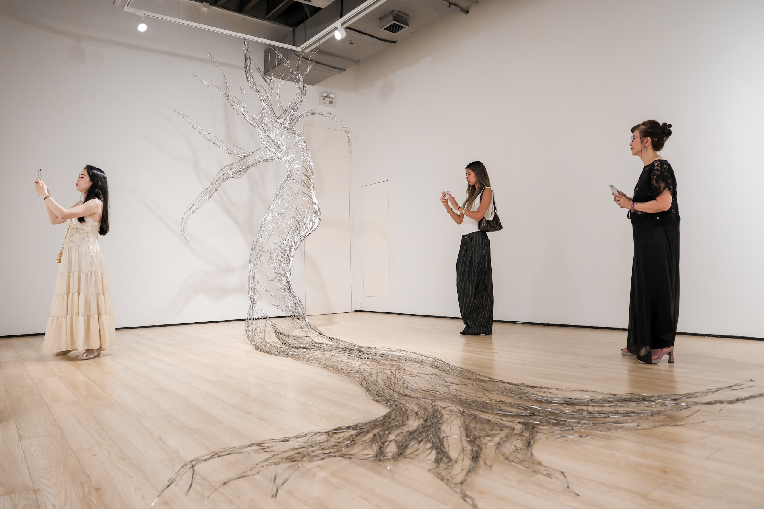 A stainless-steel tree drawn across the gallery floor and wall, with visitors