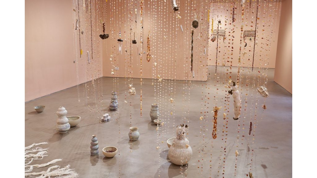 Ceramic forms on the floor beneath hanging strands