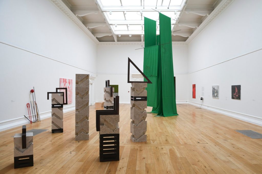 Group exhibition with green fabric hanging from the ceiling